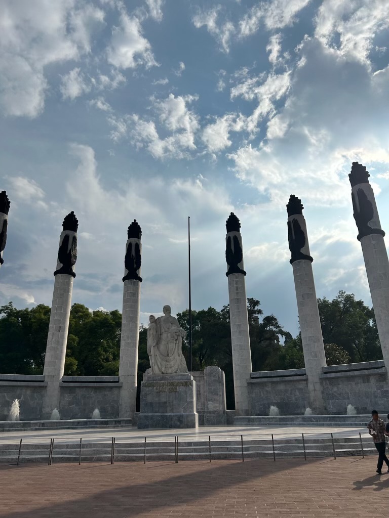 Marble columns of the Monumento a los Niños Héroes under a bright cloudy sky